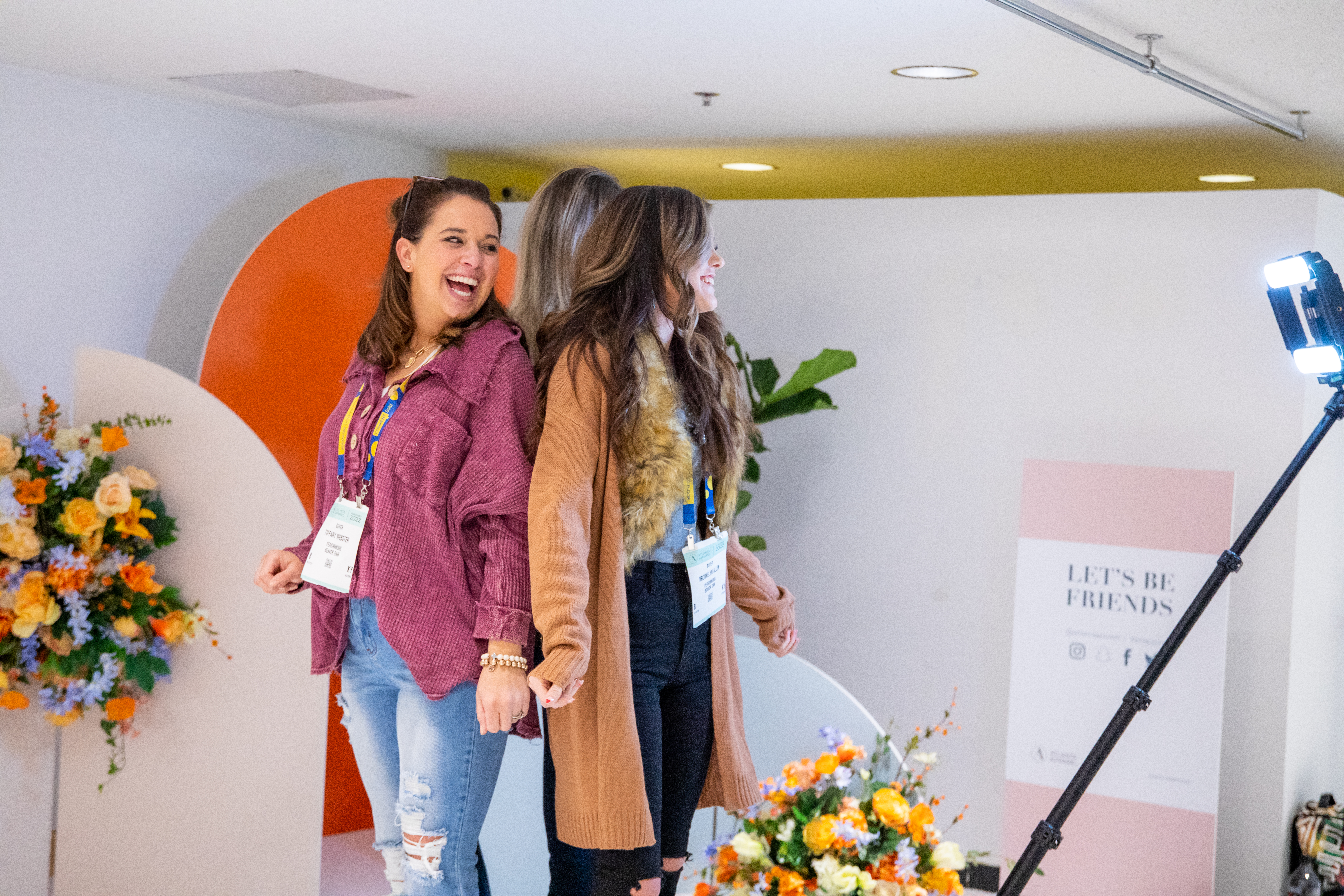 A pair of girls smiling at each other in front of an Atlanta Apparel photo display